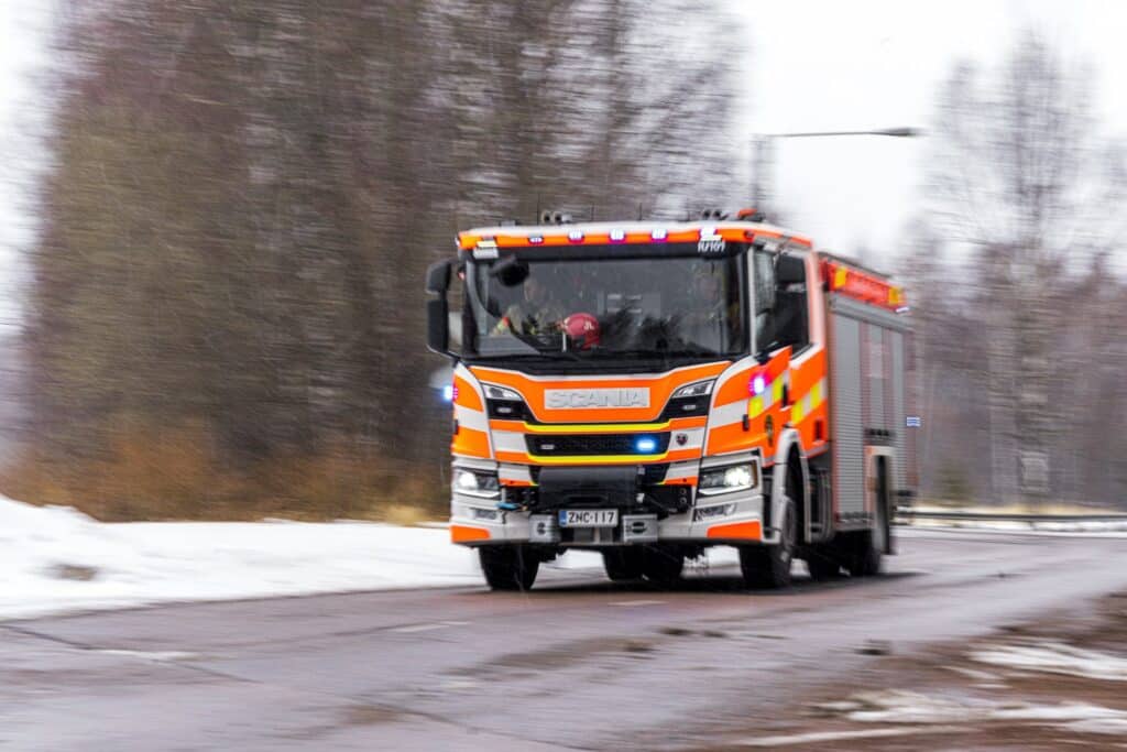 Paloauto ajaa tiellä, taustalla puita.